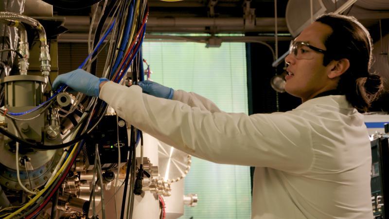 Scott Tan in profile in lab gear is working with computer wires.